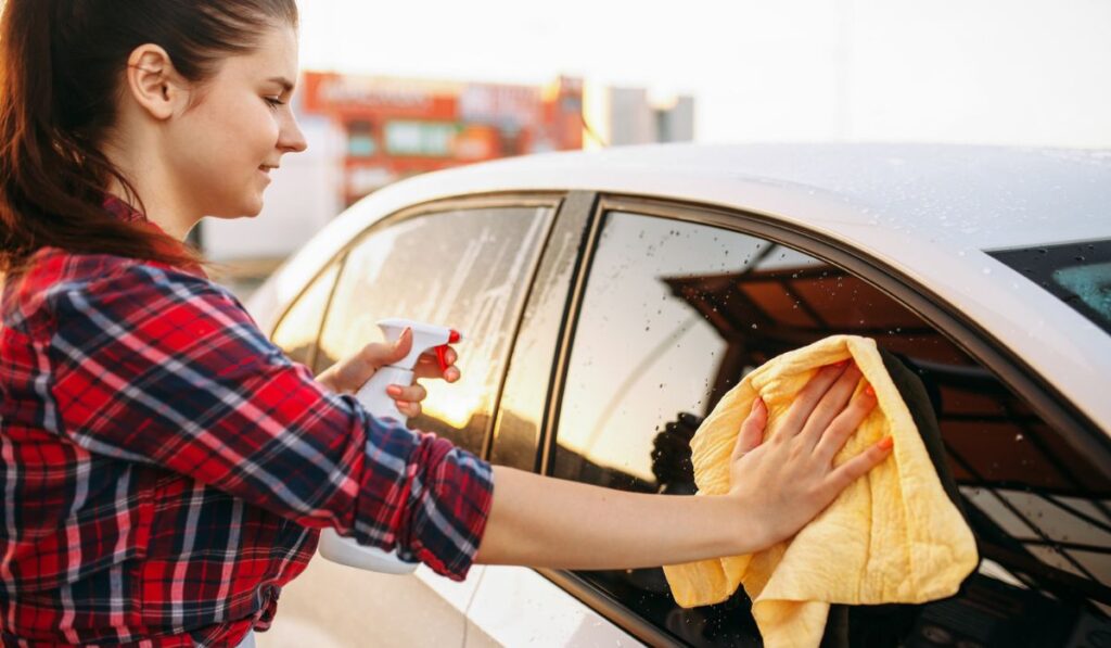 Woman cleans front glass of the car with spray