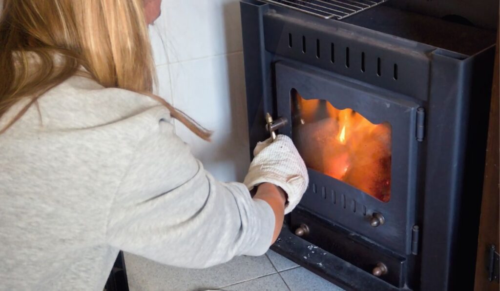 A young woman is crouching in front of a wood stove
