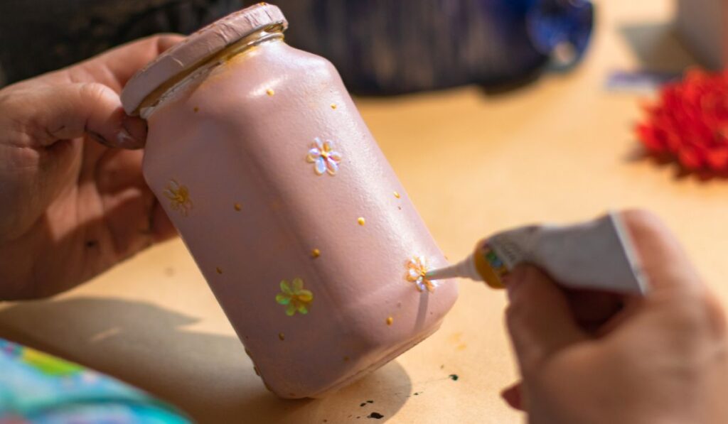 Female artist is using a glue on pink handmade glass can with a painting on it