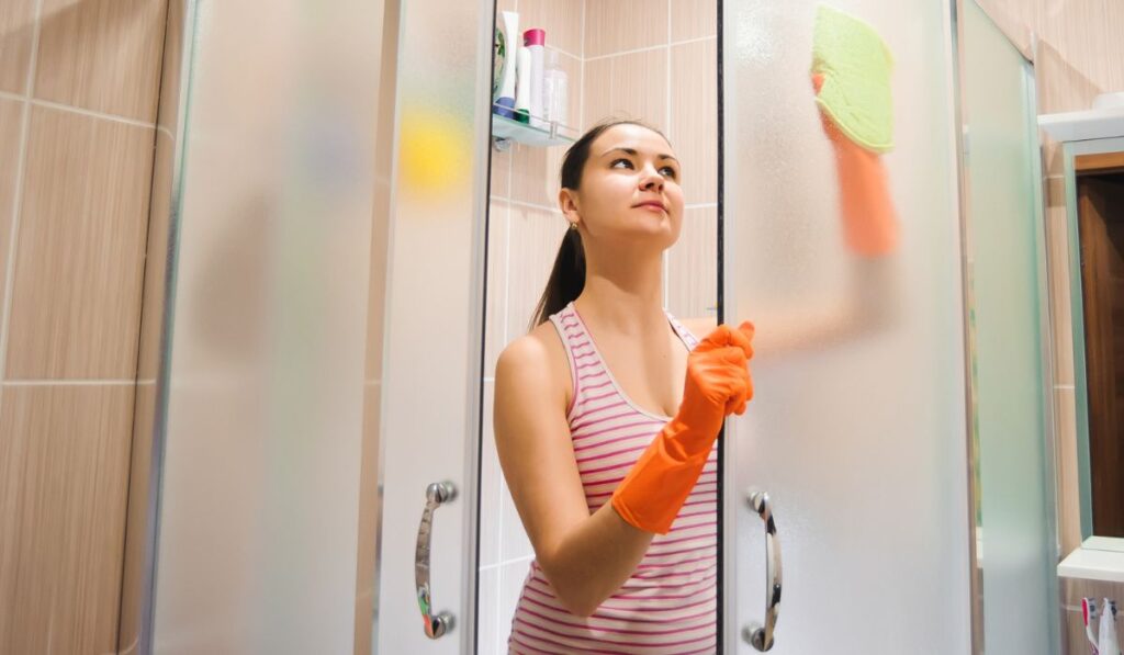 Portrait of young woman cleaning shower door
