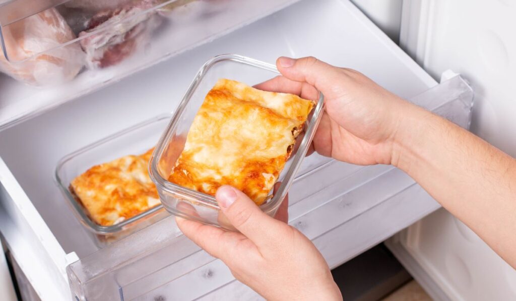 A person is taking a container of frozen casserole or lasagne out of the freezer.