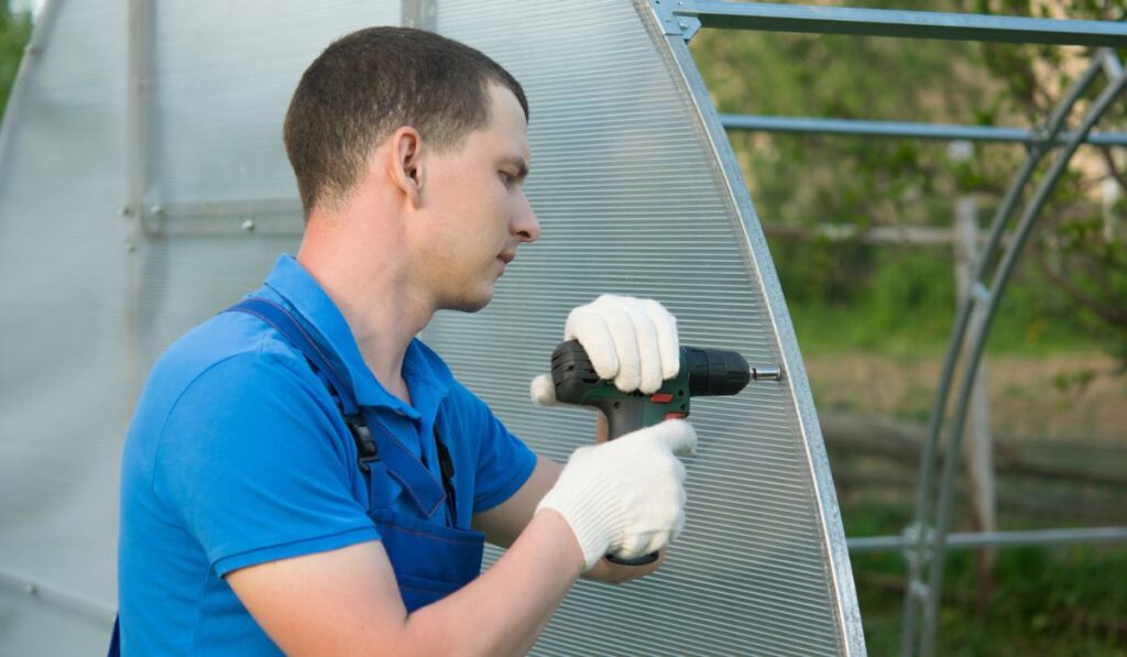 The hands of the worker twist the polycarbonate sheet with a screwdriver for installation on the greenhouse