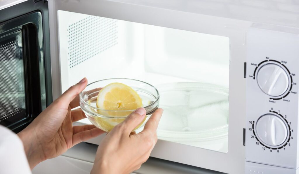 Woman Putting Bowl Of Slice Lemon In Microwave Oven