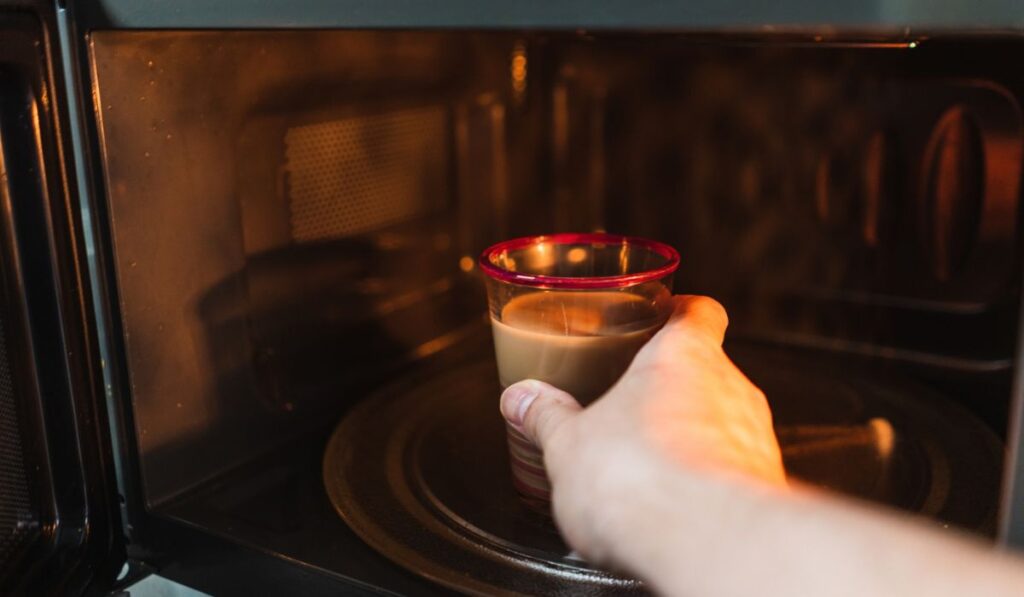 Closeup shot of a hand of the male putting a cup in the microwave to heat it