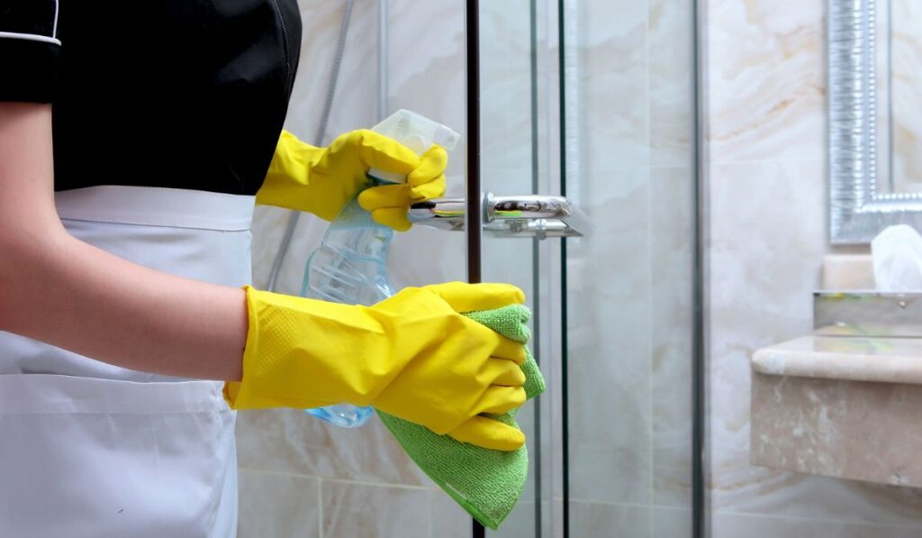 Hands in rubber gloves wash the transparent doors in the shower stall