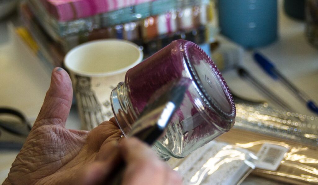 Hands painting a glass jar during crafting activity