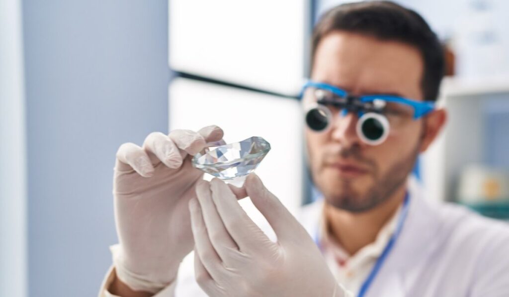 Young hispanic man scientist looking diamond by magnifying glasses at laboratory