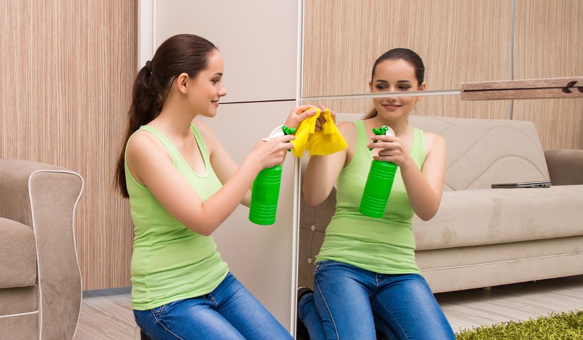 Young woman cleaning mirror at home