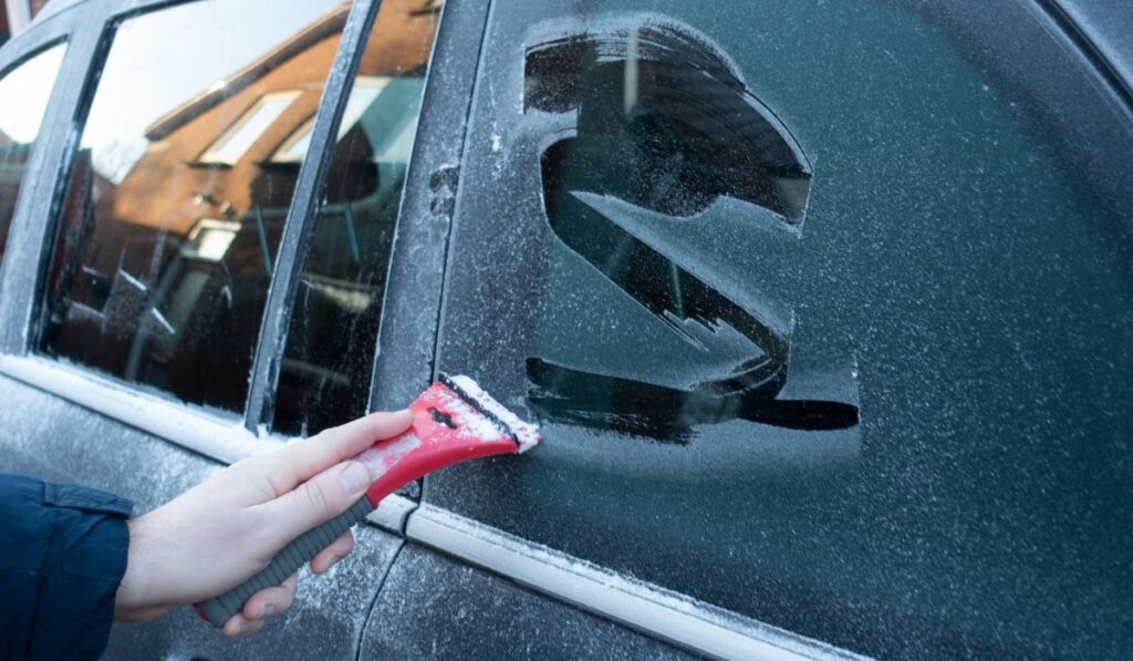 Cleaning the side car windows of snow with ice scraper before the trip