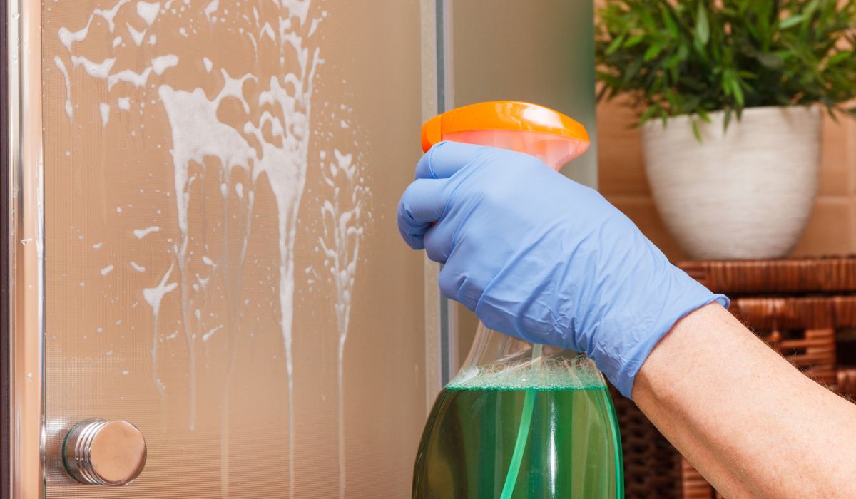 Hand of senior woman with detergent washing glass shower door