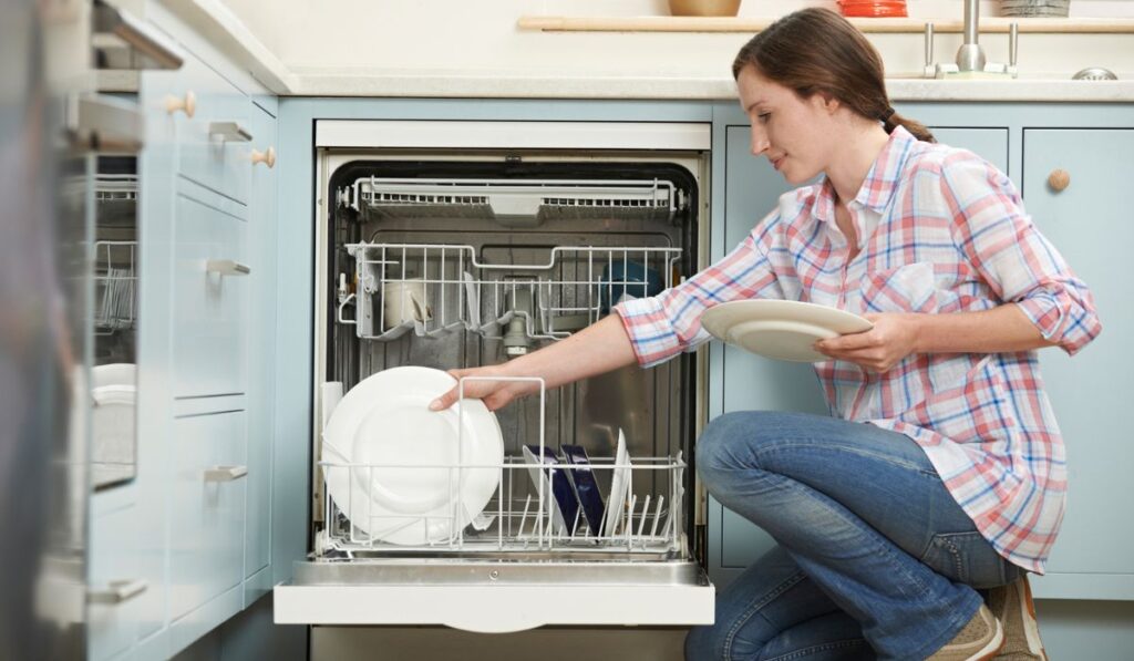 Woman Loading Dishwasher In Kitchen