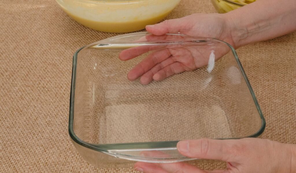 Glass baking dish in woman hands on rustic background