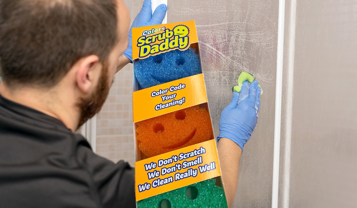 Box of scrub daddys over a picture of a man cleaning a shower door