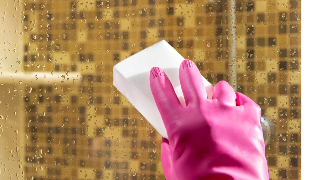 gloved hand cleaning shower door with Magic Eraser