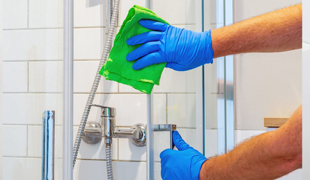 gloved hands cleaning shower door