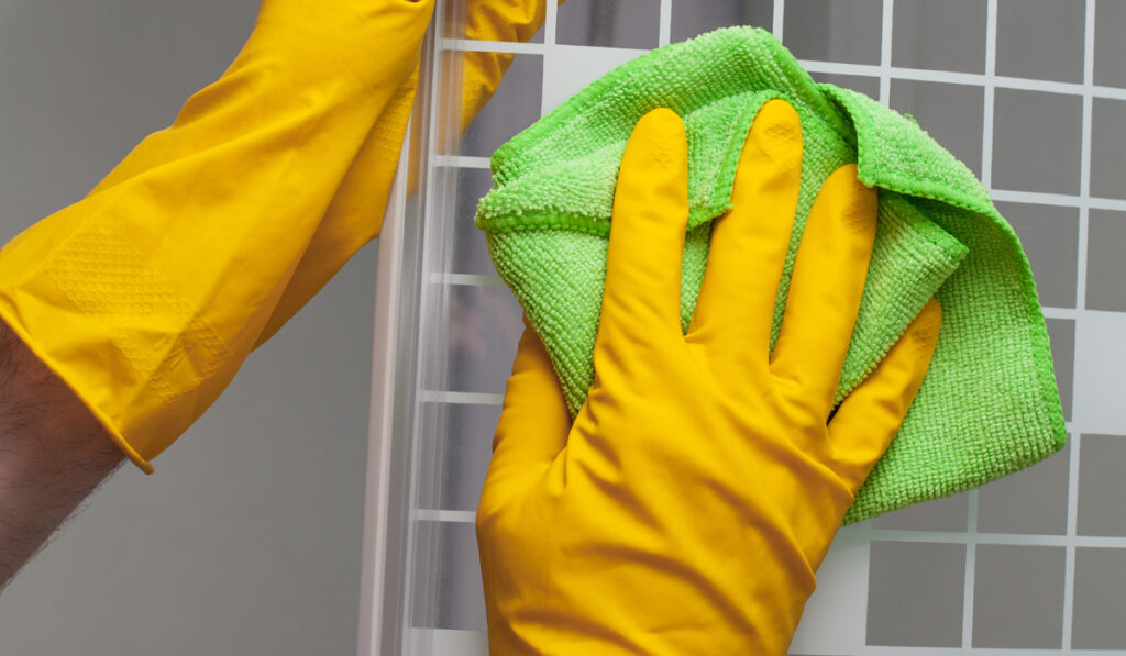 gloved hands cleaning a shower door with microfibre towel