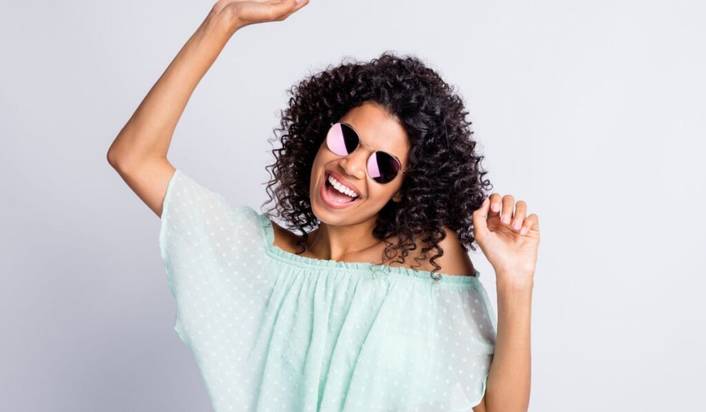 Photo portrait of happy cheerful mulatto girl with curly hairstyle wearing sunglass mint outfit dancing isolated on grey