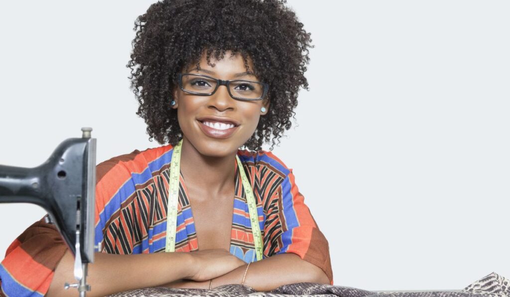 Portrait of an African American female fashion designer with sewing machine and cloth over gray background