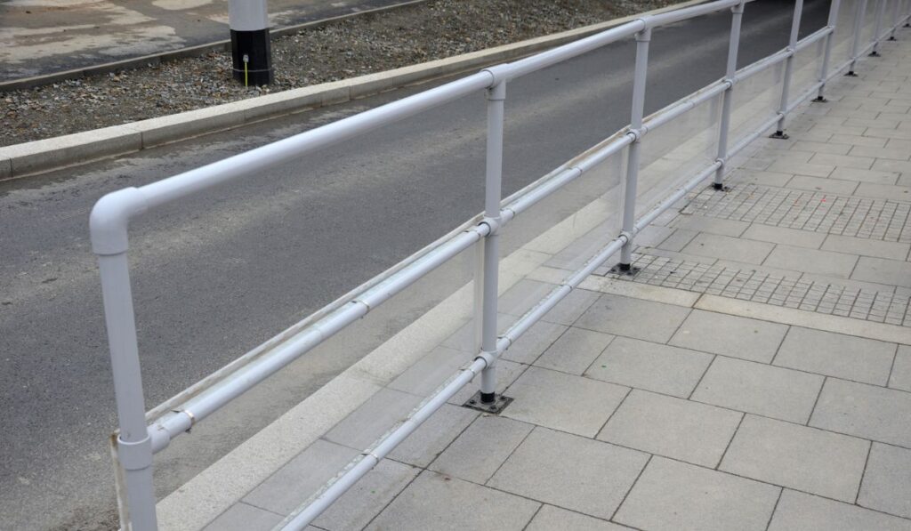 The bus platform is protected on one side by transparent plexiglass attached to a gray metal tube railing