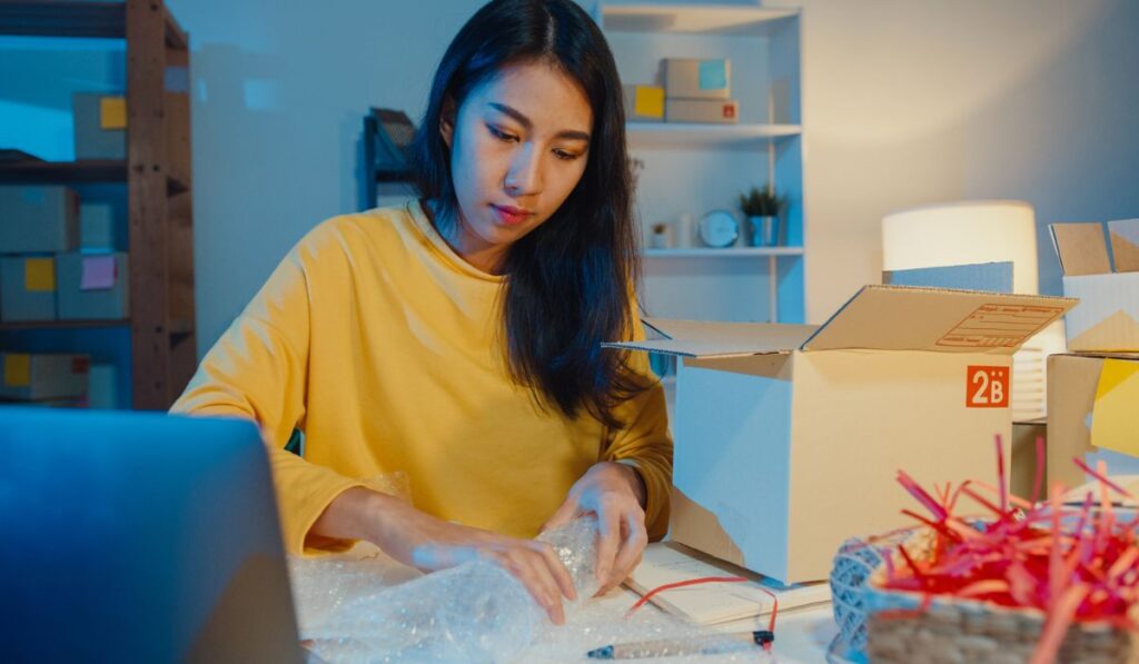 Businesswoman packing glass use bubble wrap for packing support damage fragile product in home office at night